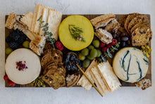 Load image into Gallery viewer, Bountiful cheese board with condiments, crackers and three cheese wheels seen from above
